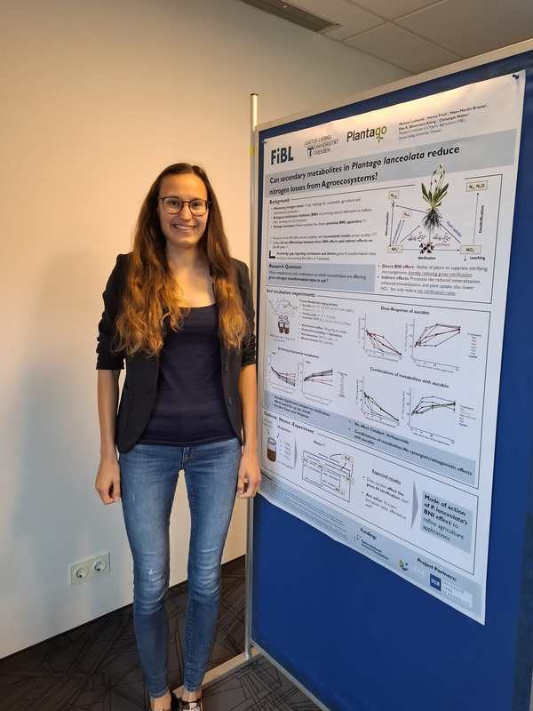 A woman stands in front of a poster, which she presents.